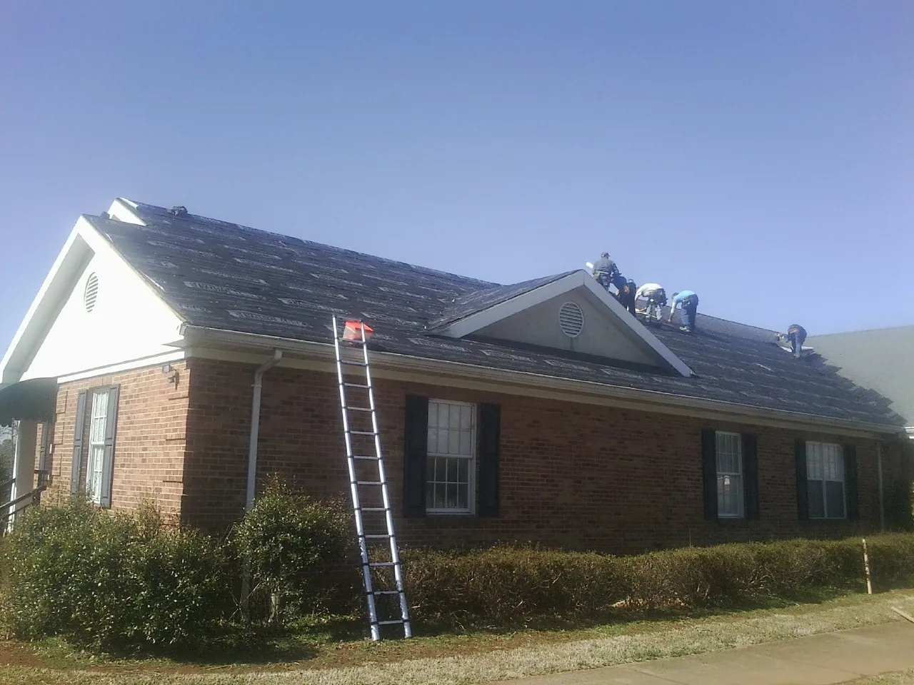 Crew tearing shingles off a brick ranch roof with a ladder set — Emergency Roof Repair work by our crew in Masonville
