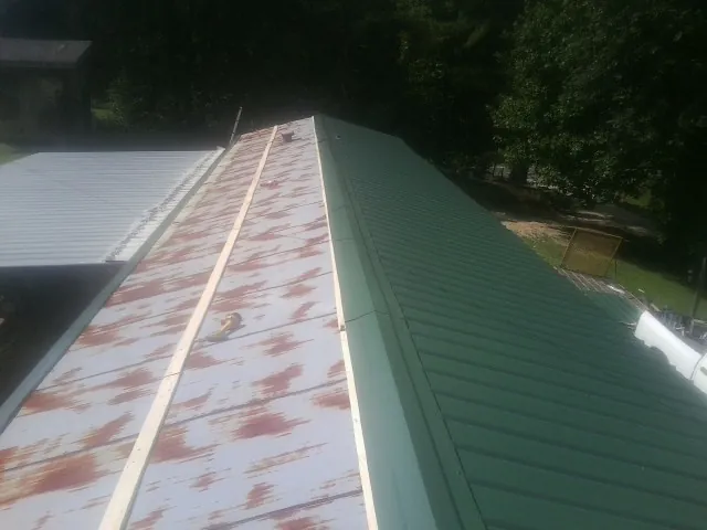 Old rusted panels beside newly installed green metal roofing — Wind Damage Roof Repair by Roofing Brothers in Masonville
