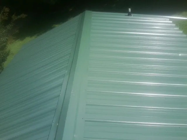 New green metal panels meeting at the ridge of a roof — Flat Roof Repair work by our crew in Masonville