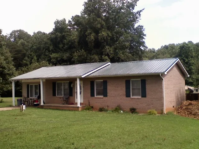 Gray metal roof on a brick ranch house with a side carport in Masonville