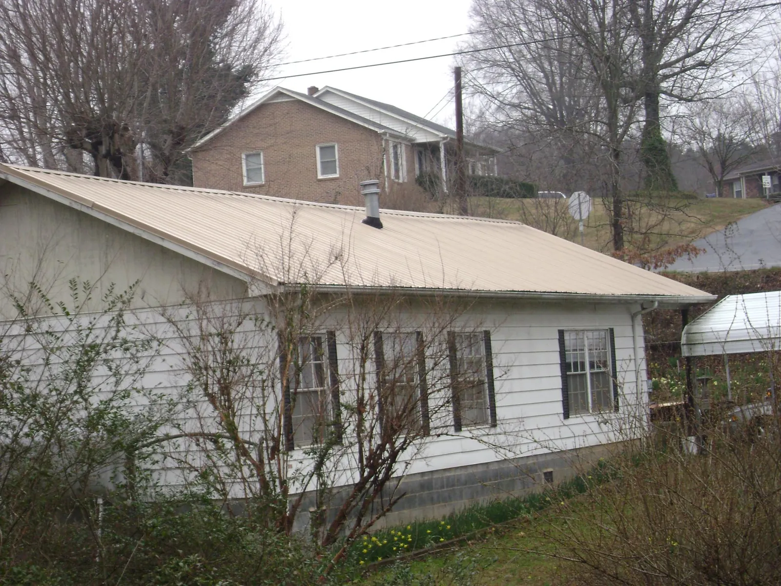 Tan metal roof on a white sided house set into a hillside — Commercial Roofing by Roofing Brothers in Masonville