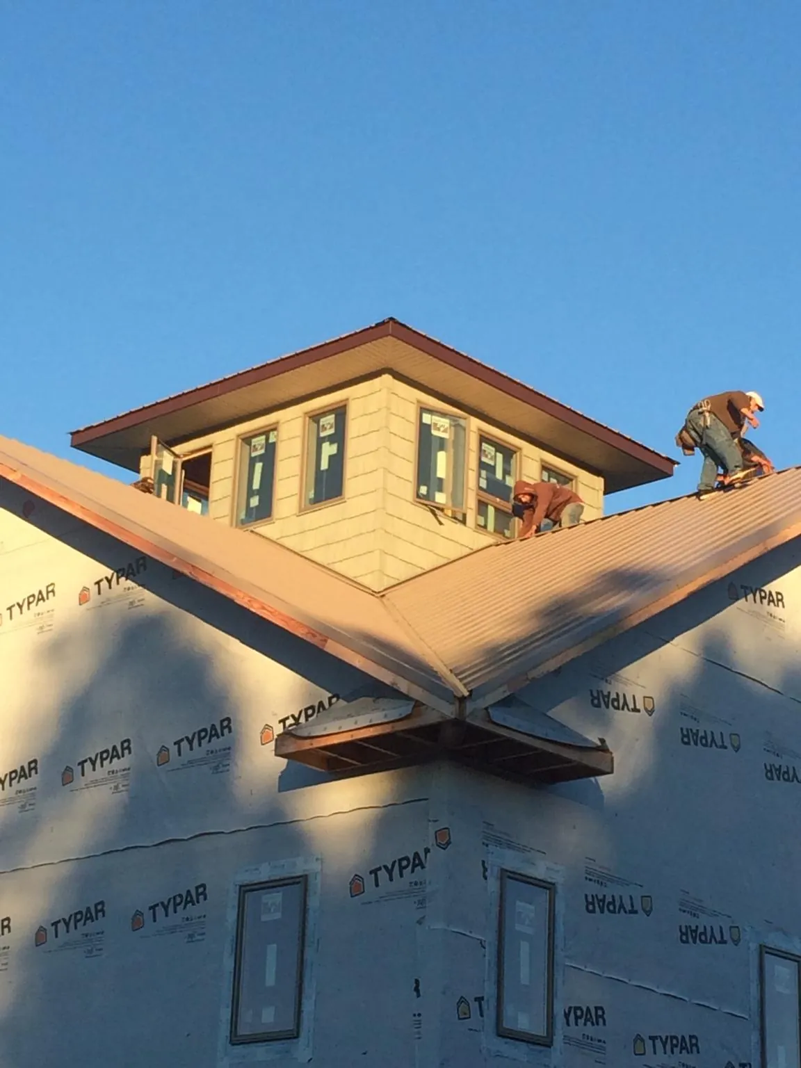 Roofers working around a rooftop cupola on a new metal roof at sunset — Roof Waterproofing in Masonville by Roofing Brothers